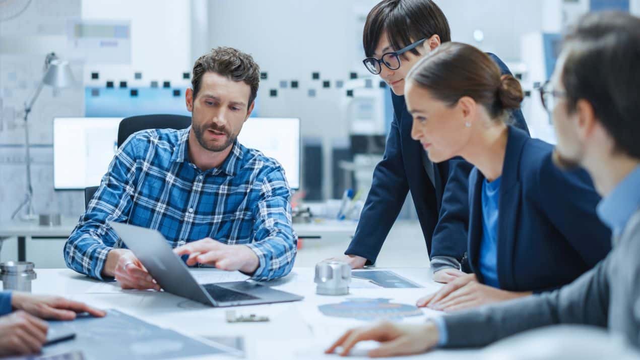 Mitarbeiter in einem Meeting, die mit Laptops und Plänen digitale Strategien zur ERP Metallverarbeitung besprechen.