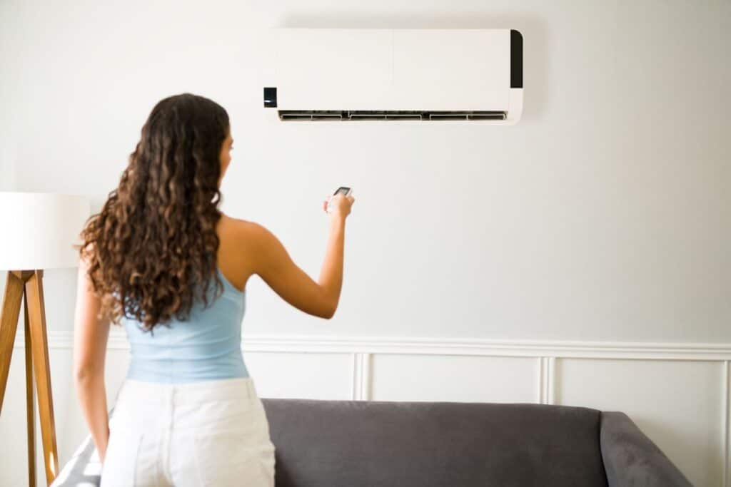 Back view of a woman holding a remote control to adjust a wall-mounted air conditioner in a living room