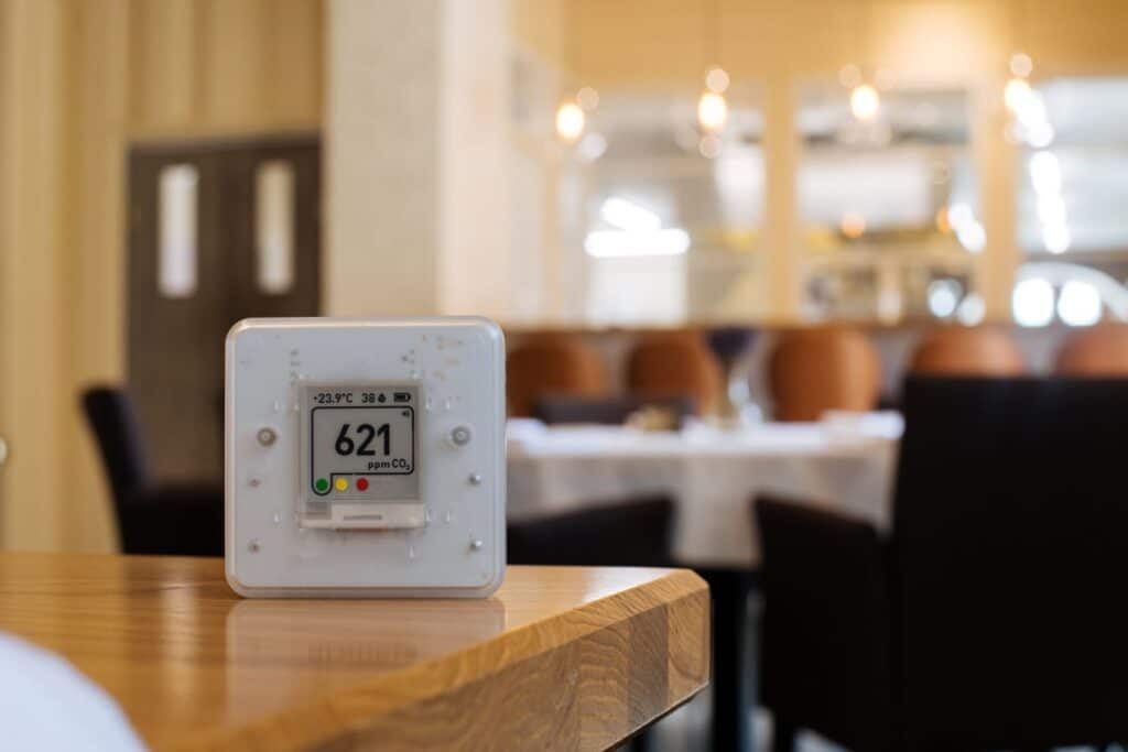 CO₂ sensor showing air quality levels and temperature on a wooden table 