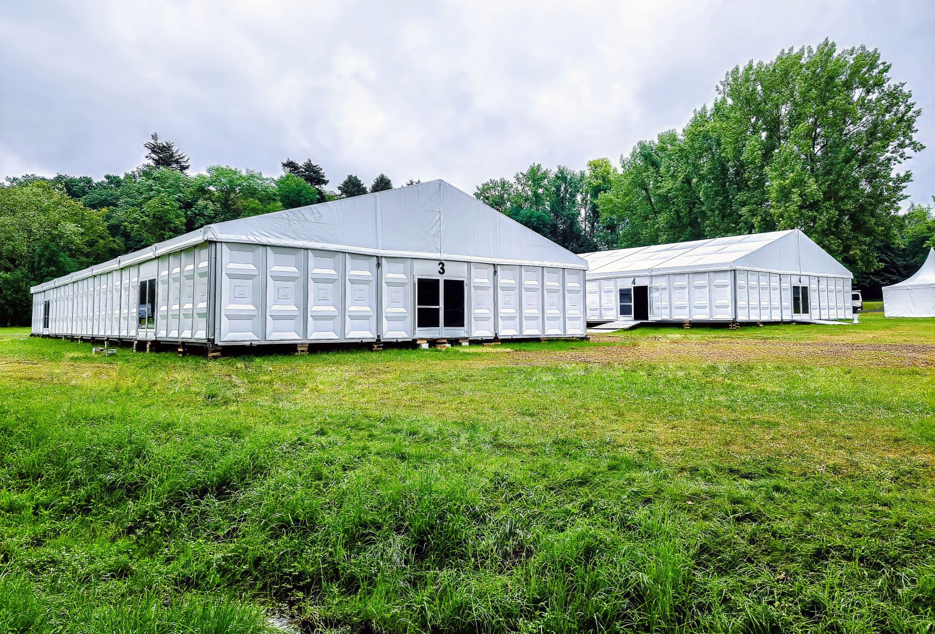 Grosse modulare Eventzelte auf Wiese mit Tueren und Seitenwaenden, aufgebaut fuer Veranstaltung im Gruenen